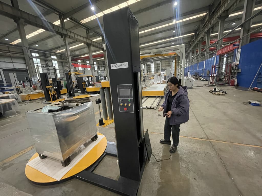 Sinospect-branded automatic pallet stretch-wrapping machine on the factory floor with an engineer operating the controls — equipment commissioning and operator validation context.