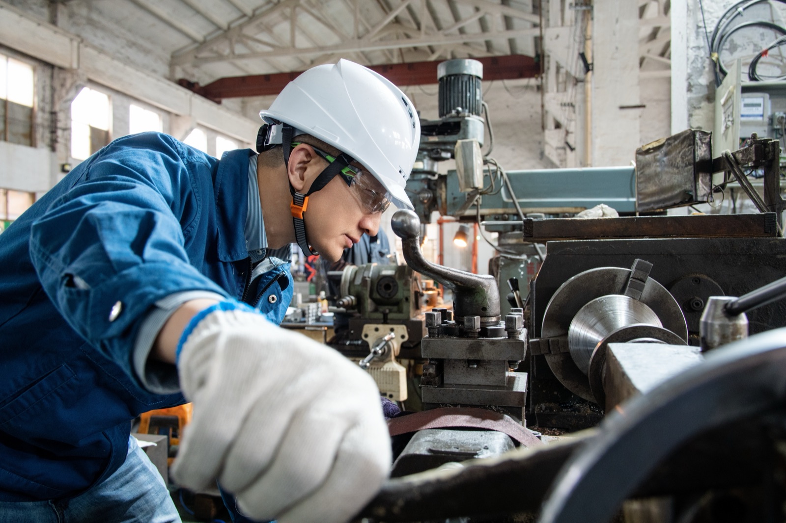 Machinist shaping a metal part on a manual lathe in a China tooling workshop.